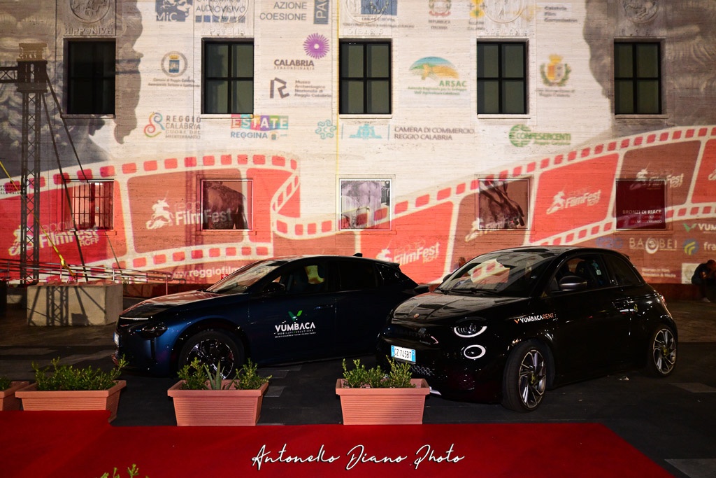 Red carpet del Reggio Calabria Film Fest: due auto sul tappeto rosso davanti alla facciata su cui è proiettata la grafica del festival.